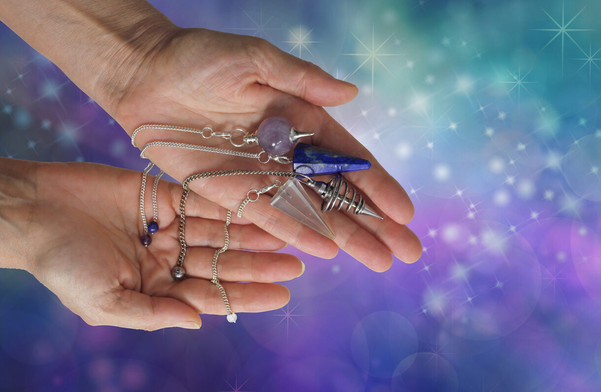 Hands holding several pendulums-used to unlock your inner wisdom
