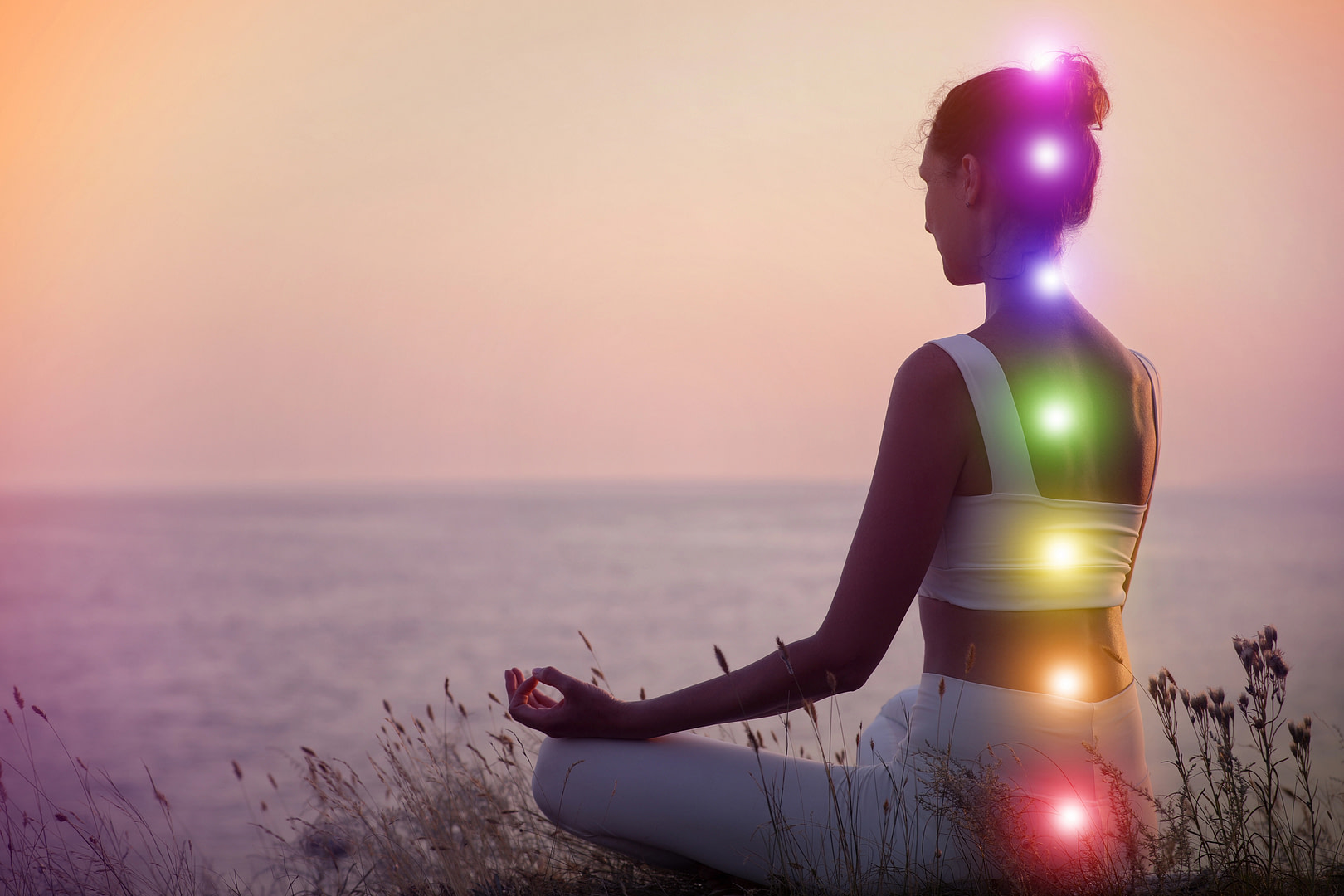 Woman meditating by the water with the 7 chakras lit up along her body