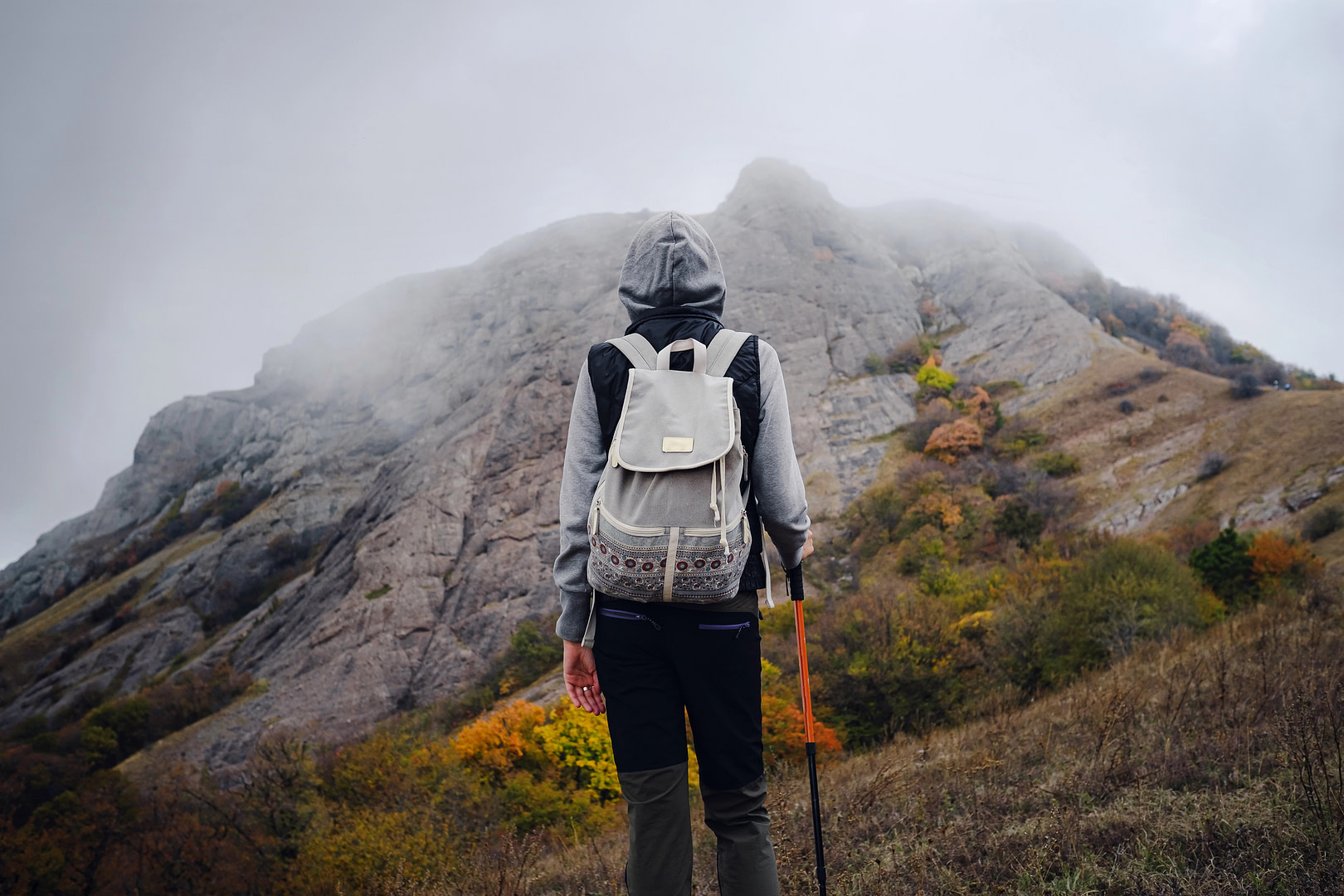 Woman standing on the ground in front of a mountain. Cold weather, fog on the hills. Represents navigating through life’s uncertainties.