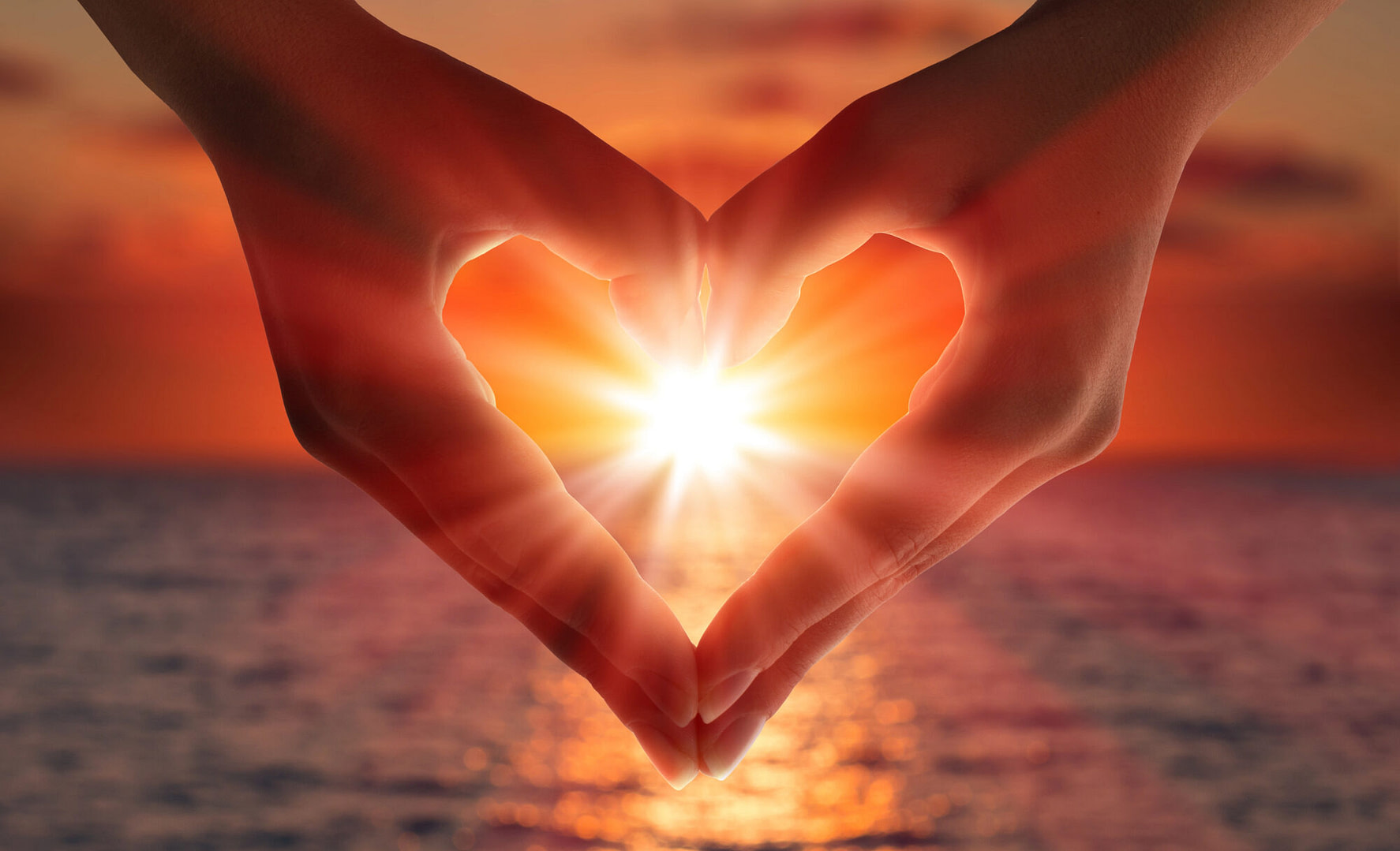 Sunset over the water in heart hands