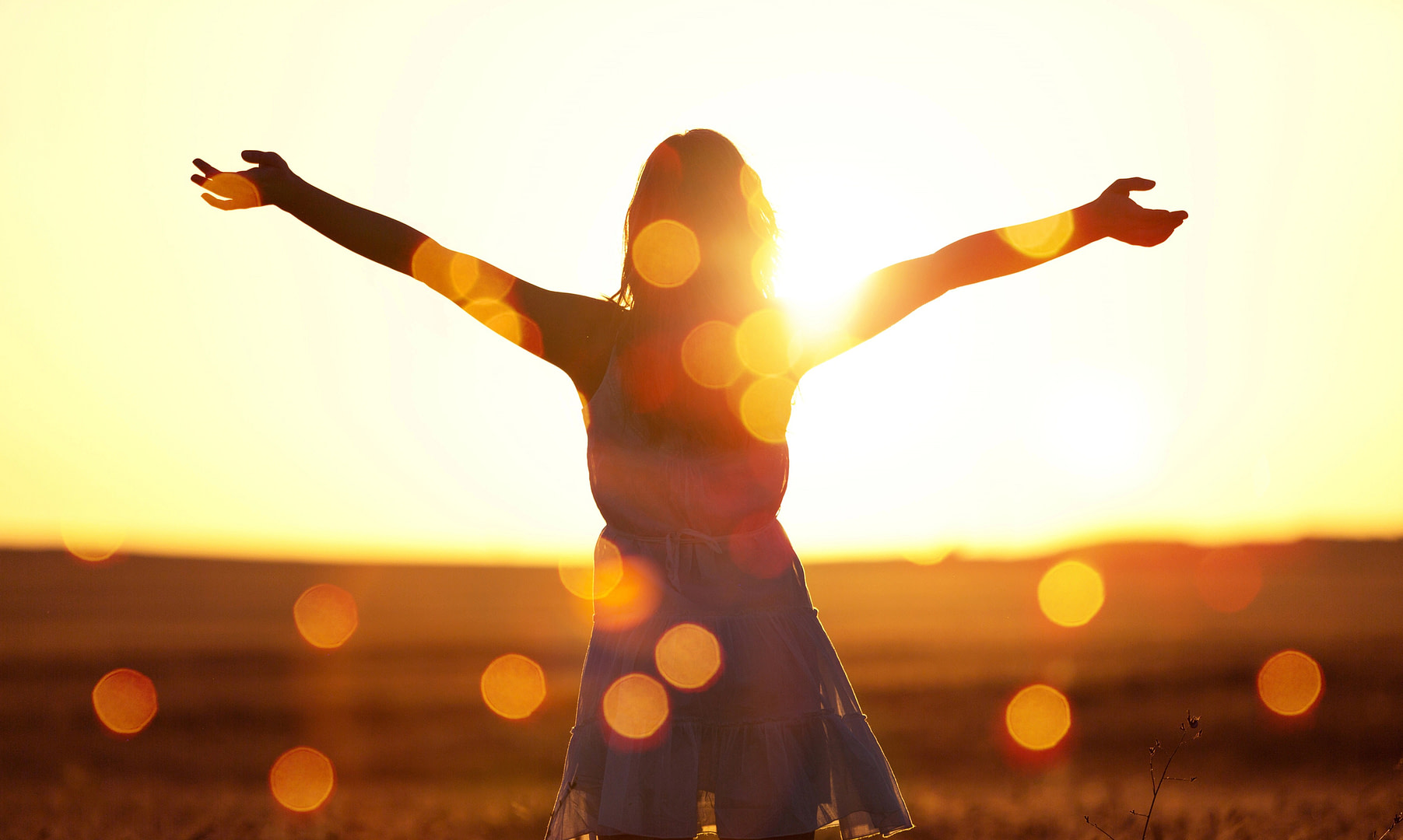 Woman with arms outstretched at sunset to represent living life to the fullest