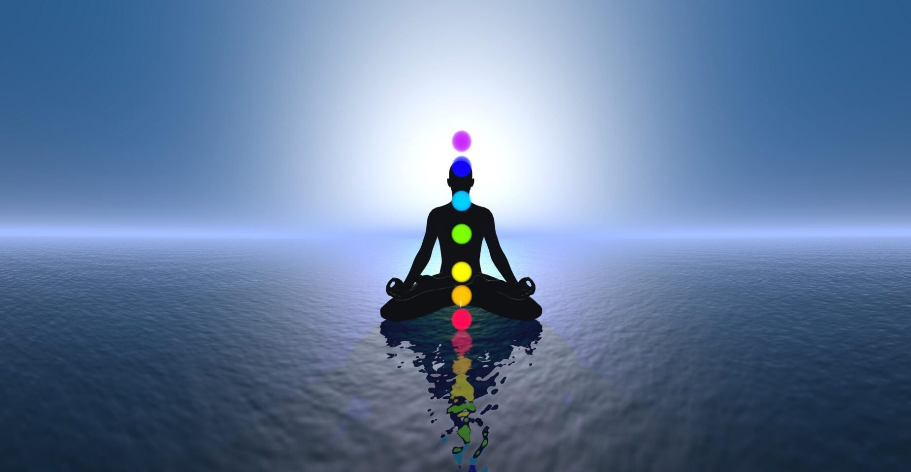silhouette of man in lotus pose on the water with colored chakras lit up