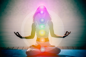 Woman working to balance her energy. Sitting in lotus pose with chakra lit up along the body.