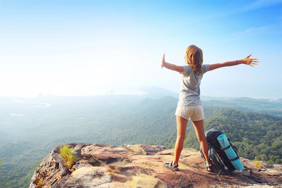 Light and Free female with bag set down on a rock overlooking landscape arms outstretched