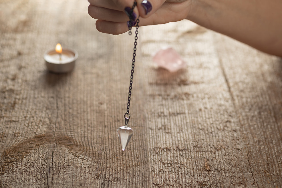 Hand holding natural crystal pendulum on chain Hand holding pendulum on a chain with a natural crystal on a background of wood