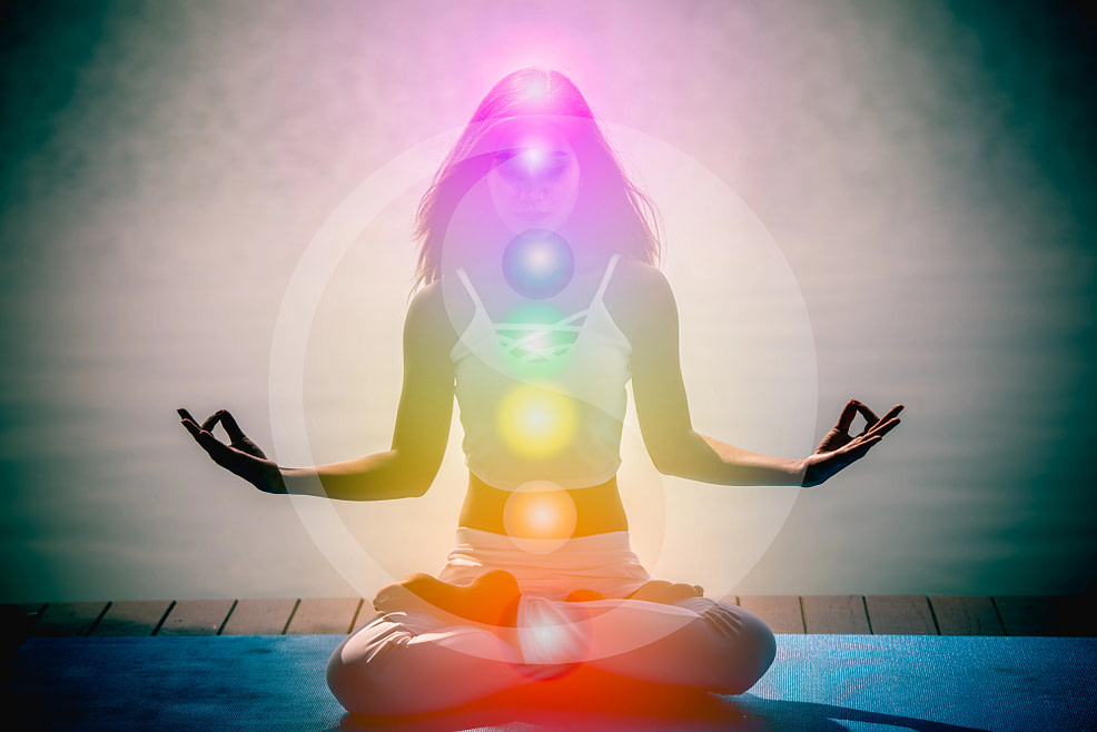 Seeing the Energy Woman working to balance her energy. Sitting in lotus pose with chakra lit up along the body.