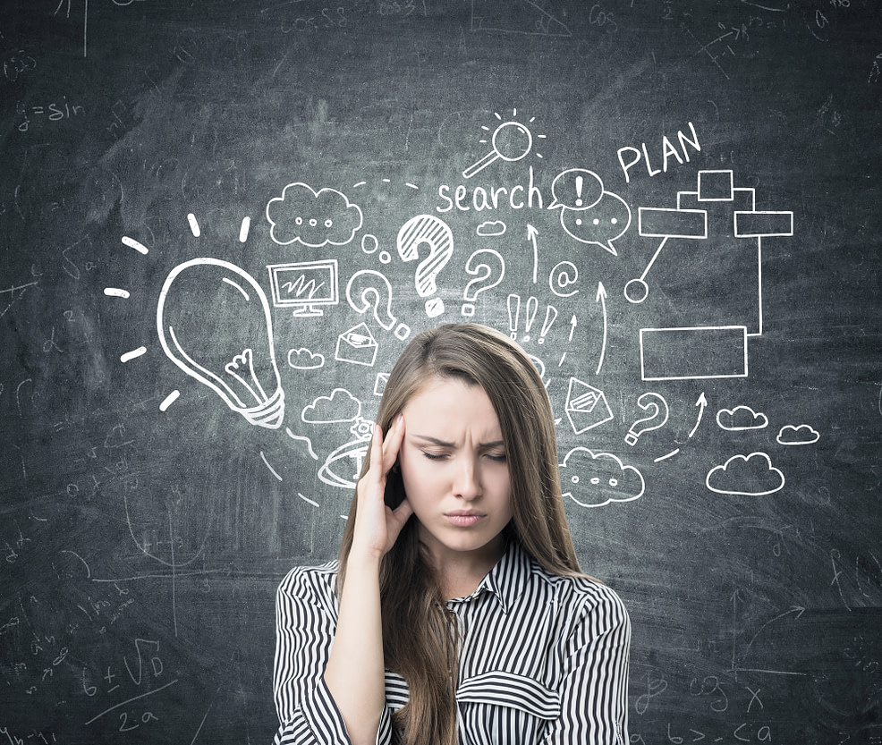 Stressed woman standing in front of chalkboard with lightbulbs and question marks trying to figure out a plan. Representing the brain’s fight for control during life’s uncertainties.