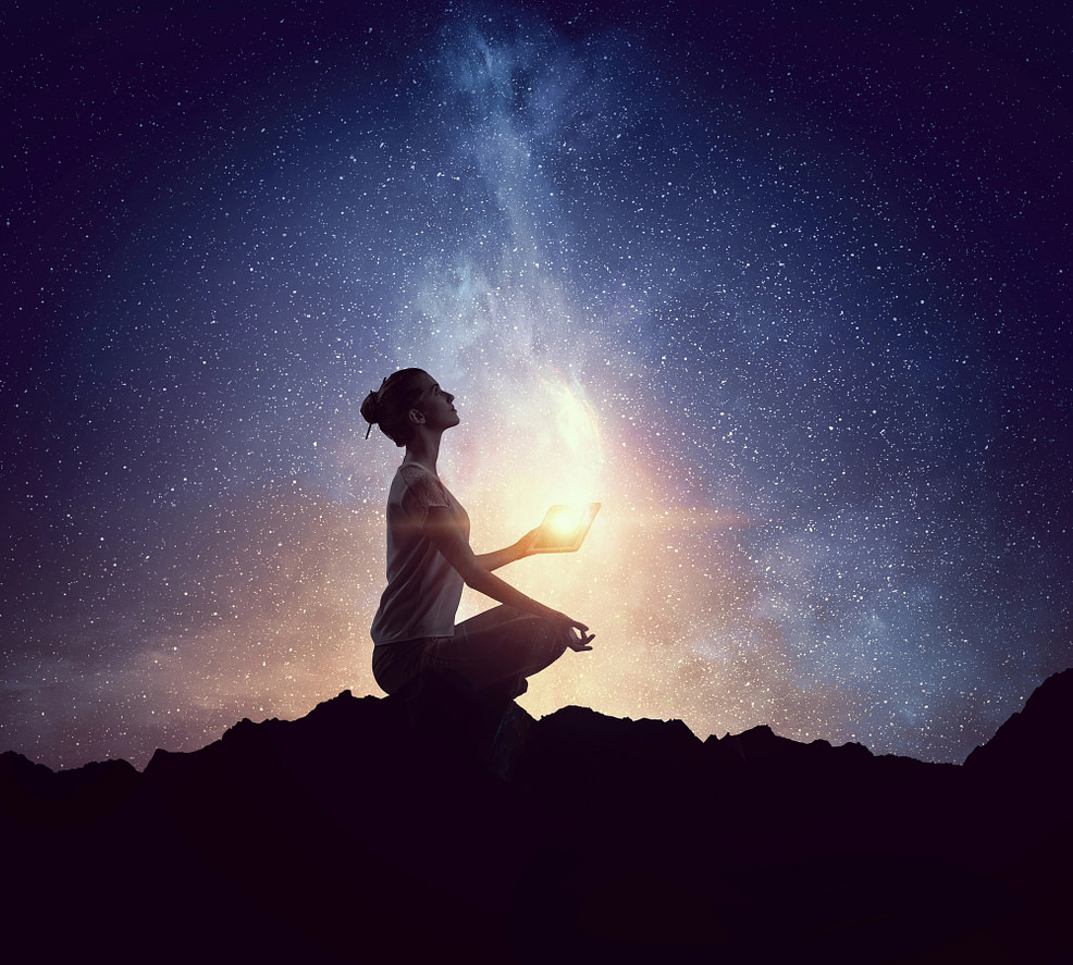 Manifesting Magic female sitting in lotus pose with dark blue starry sky reflecting light from hand