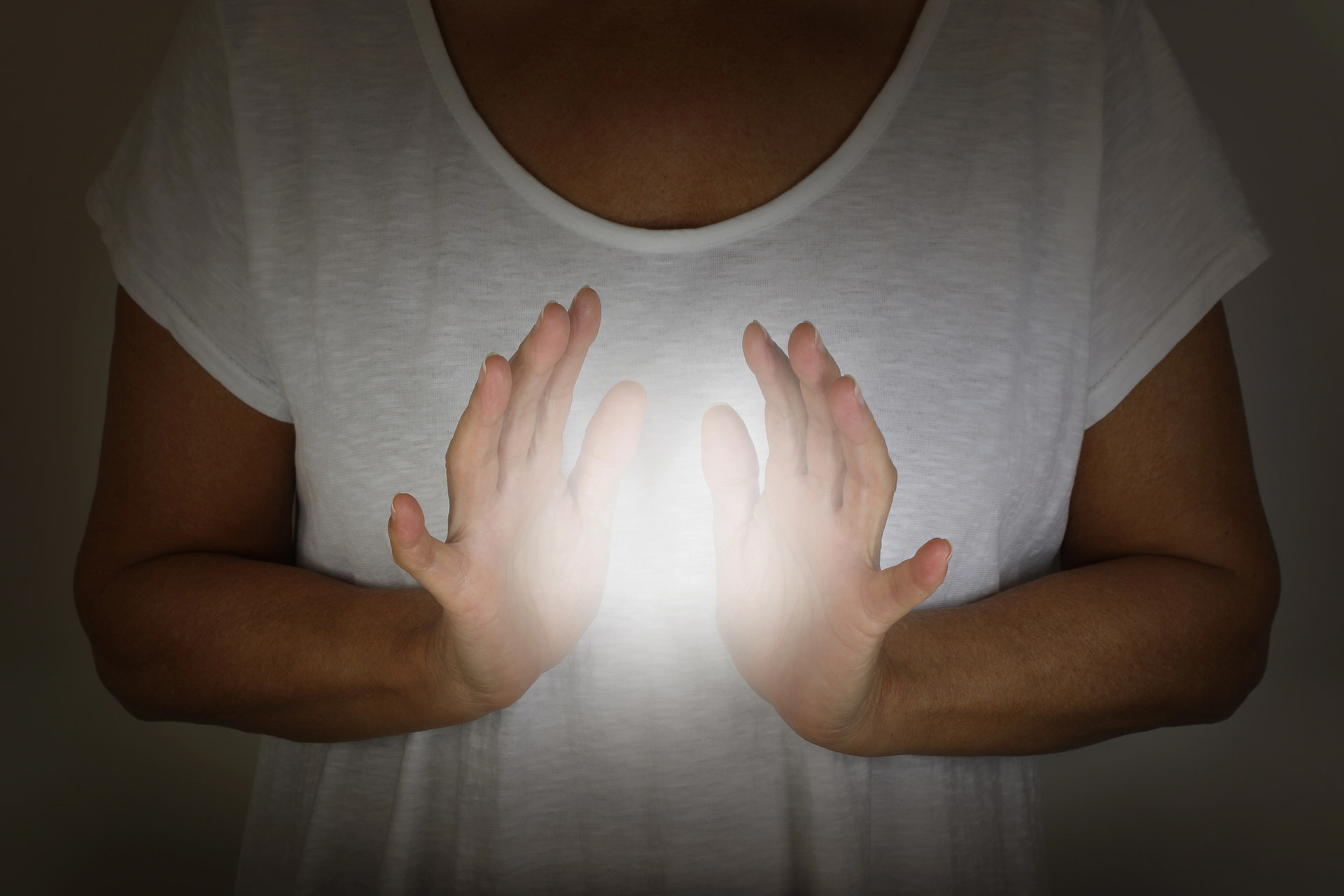 female in white tunic with hands apart at chest level with a bright shining white orb light between