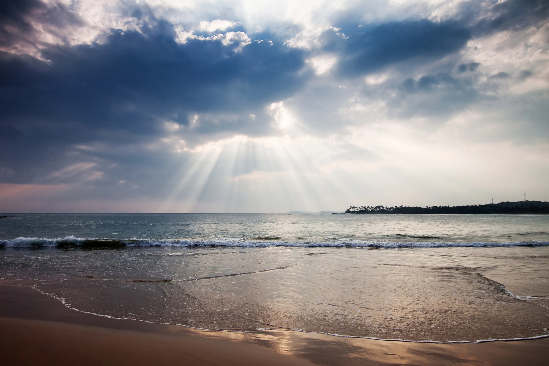 Beach with rays of sun shining on the water through the clouds