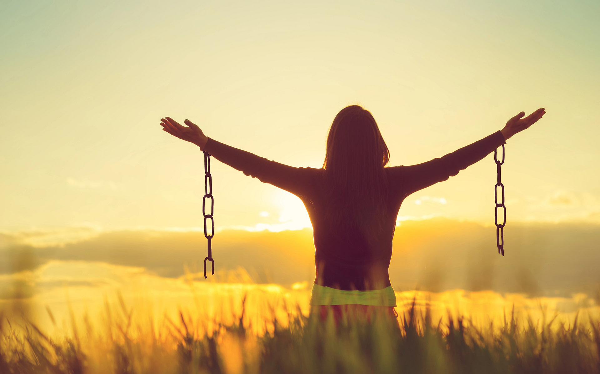Woman outside with hands outstretched and chains hanging from wrists, freedom concept
