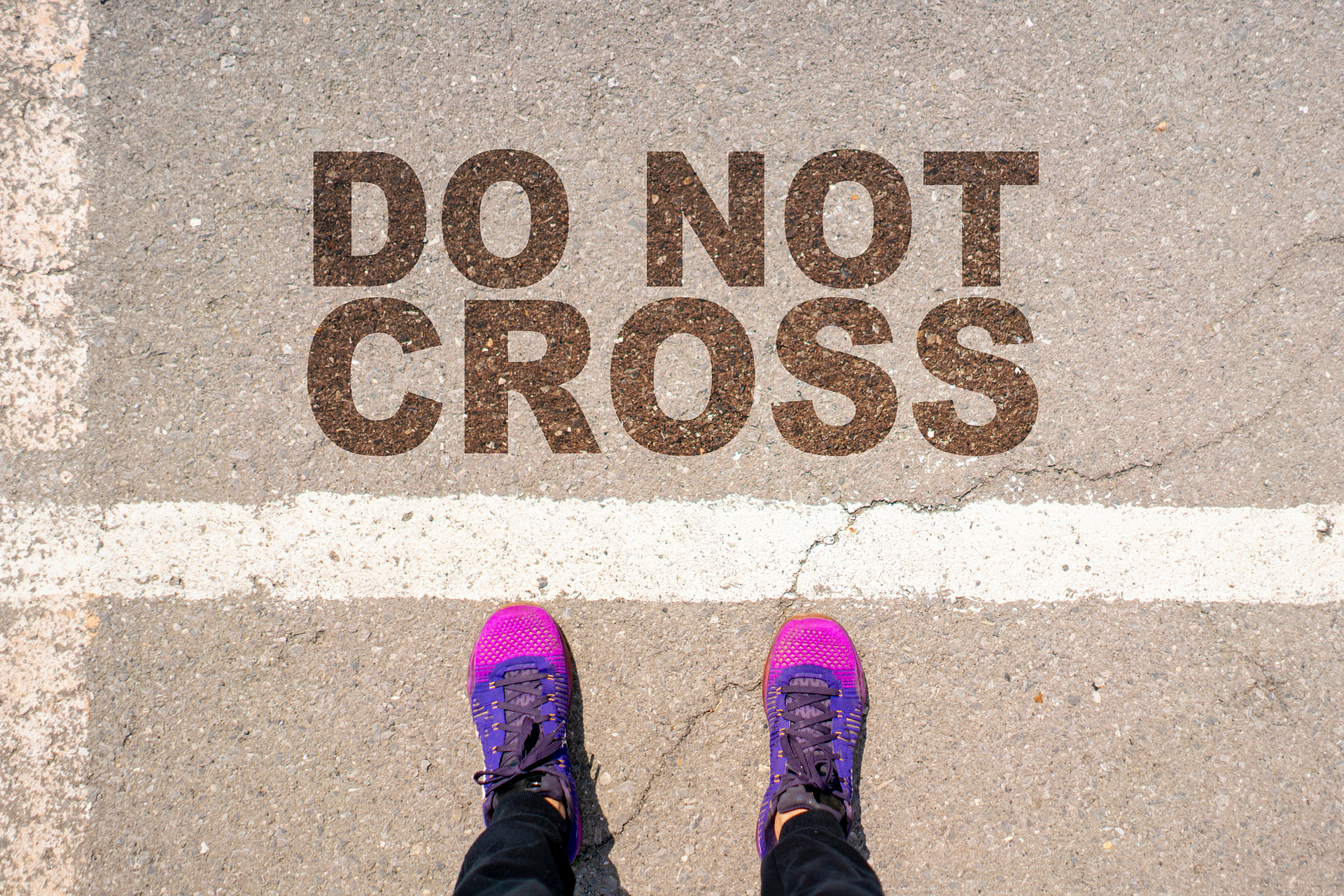 Top down view of feet standing on the ground behind a line that says do not cross