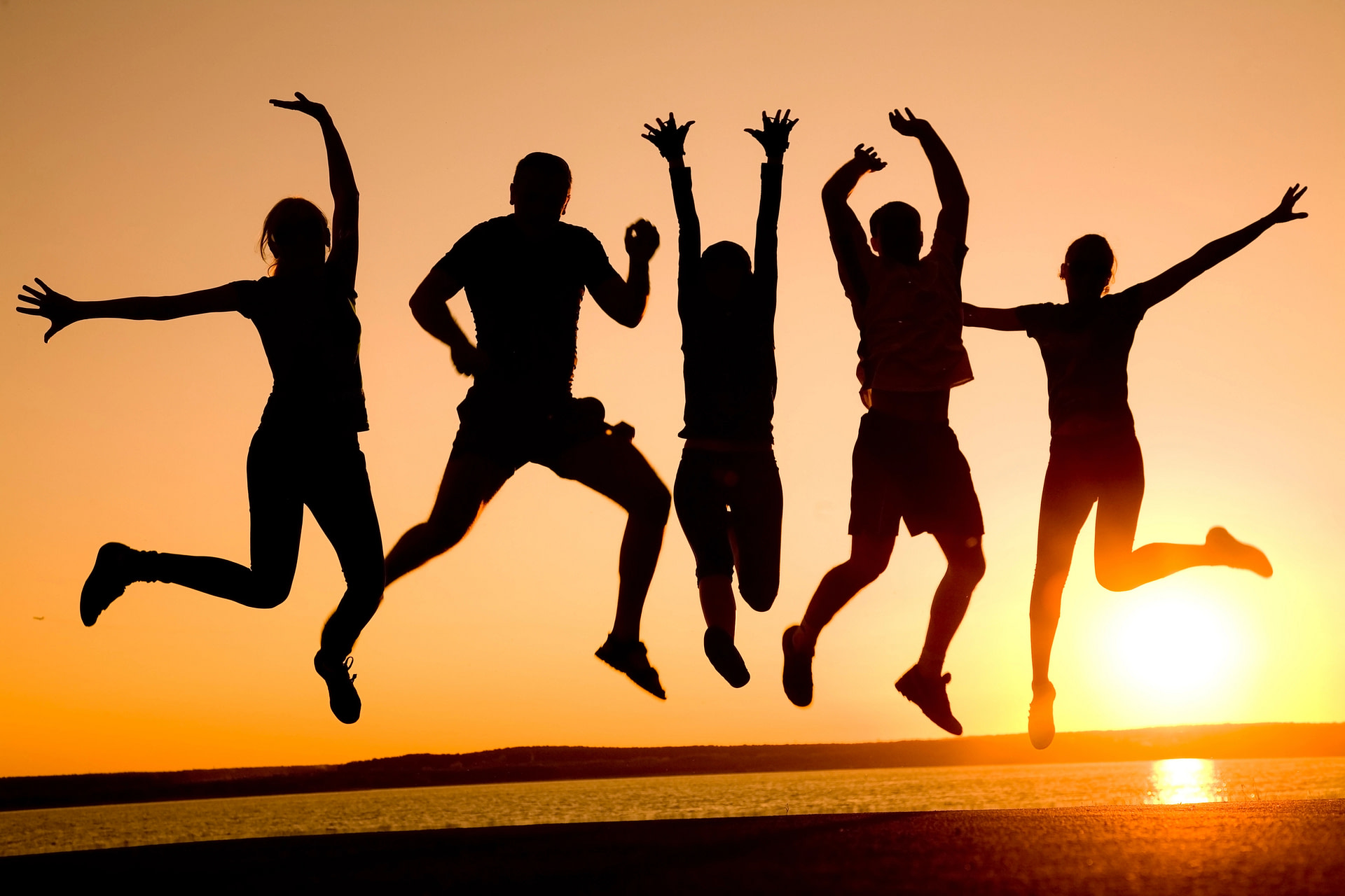 sillhouette of 5 people in jumping in the air at sunset on a beach, living life to the fullest in connection